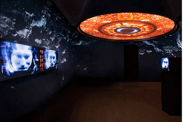 Left: Marco Brambilla, Countdown (Apollo XVIII), 2015, Dual-screen video tile display in powder-coated custom enclosure with playback unit, 2:30s 4K color, sound, Edition of 3; Middle: Marco Brambilla, Ignition (Apollo XIII), 2015, Circular projection; Right: Marco Brambilla, Transmission - Frank Borman (Apollo VIII), 2015, Video display, powder-coated metal plinth with playback unit; Background: Marco Brambilla, Reconnaissance (Apollo VIII), 2015, Black and white photographic wallpaper